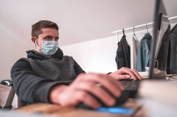Active teen Boy in face mask with laptop homework during a coronavirus quarantine. concept of online education. Social distance, self- isolation. Distance learning due to virus, flu, epidemic COVID-19 - Foto, afbeelding