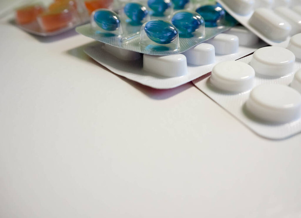 Verpakkingen van tabletten ovaal en rond in witte, blauwe en oranje kleuren op een lichte achtergrond - Foto, afbeelding