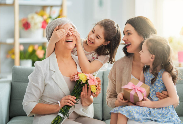 Happy mother's day! Children daughters are congratulating mom and granny giving them flowers and gift. Grandma, mum and girls smiling and hugging. Family holiday and togetherness.        - Fotografie, Obrázek