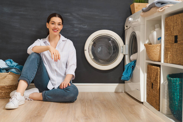 Beautiful young woman is smiling while doing laundry at home.                                 - Foto, Imagem