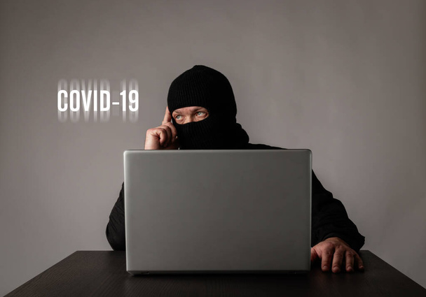 テロリストは、 COVID-19コロナウイルス発生の間、自宅に滞在しています。隔離の概念。ネットを閲覧するためにラップトップを使用してマスクの男. - 写真・画像