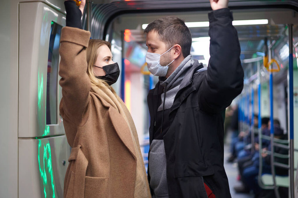 Man and woman in medical masks holding handrails in subway car - Fotografie, Obrázek