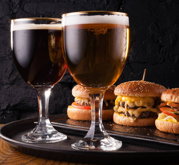 Birra fredda in un bicchiere e uno spuntino sotto forma di grandi hamburger succosi. Fast food
. - Foto, immagini