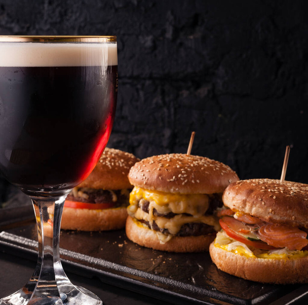 Cold beer in a glass and a snack in the form of juicy large burgers. Fast food. - Foto, afbeelding