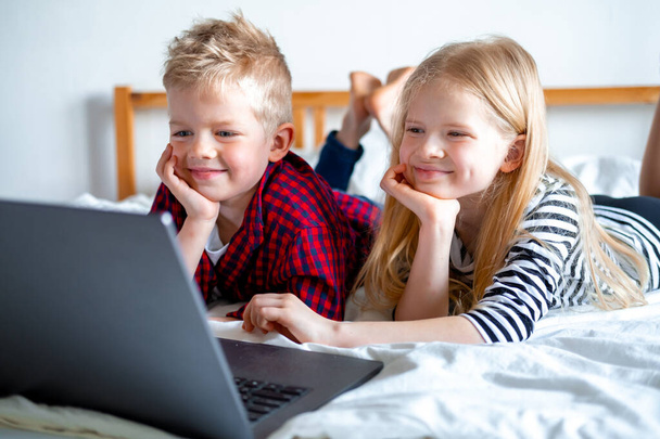 Distance learning online education. Schoolboy and girl studying at home with digital tablet laptop notebook and doing school homework. Sitting on bed with training books. - Zdjęcie, obraz