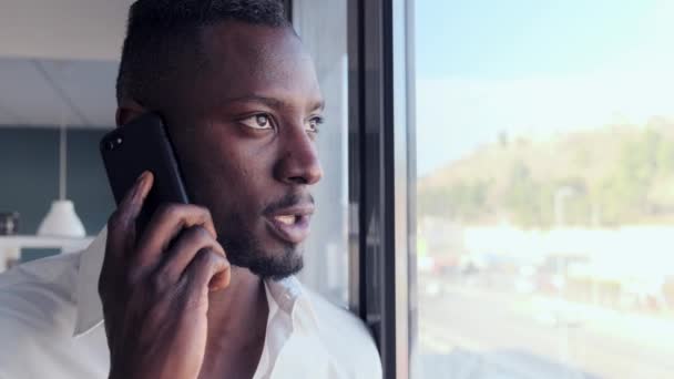 Obchodní mladý muž mluví na mobilním telefonu, zatímco se dívá oknem v kanceláři. - Záběry, video