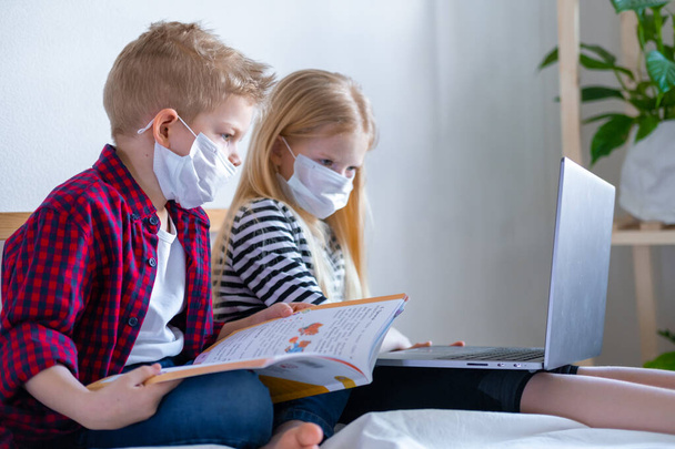 Distance learning online education. Sickness school boy and girl in medical mask studying at home with digital tablet laptop notebook and doing homework. Sitting on bed with training books - Photo, Image