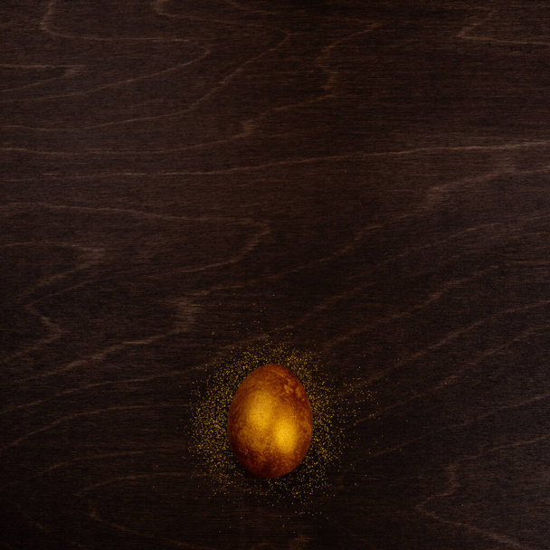 One big golden easter egg on dark wooden background copy space for text - Foto, Imagem