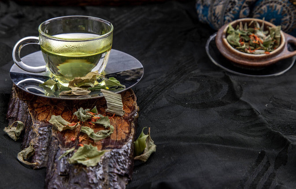 Una taza de té de hojas de pandan, hojas de pulgas de pantano indio con cártamo seco (sustituto del azafrán) en el fondo oscuro. Planta de hierbas tailandesa y concepto de bebidas saludables. Enfoque selectivo
. - Foto, Imagen