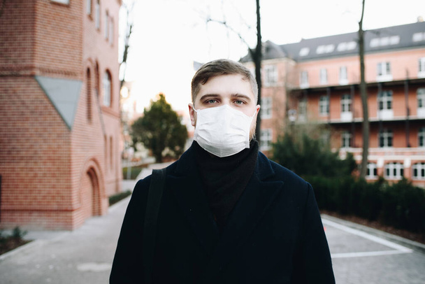 Młody przystojny mężczyzna idzie z maską na twarzy w dzielnicy mieszkalnej podczas covid-19 coronavirus globalnej pandemii i kwarantanny - Zdjęcie, obraz