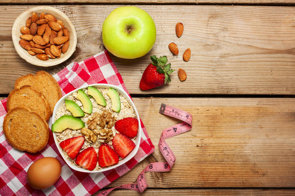 Gezond ontbijt gemaakt van haver met noten, avocado en verse aardbeien en fruit op houten tafel, kopieer ruimte in het midden - Foto, afbeelding