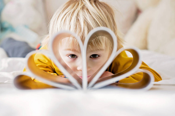 Beautiful child, toddler boy, reading book and playing with it, creative knowledge shot with book and letters - Photo, Image