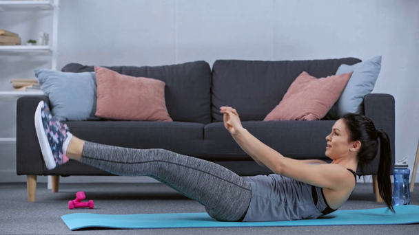 Vista lateral de la deportista haciendo abdominales en la alfombra de fitness en la sala de estar
  - Metraje, vídeo