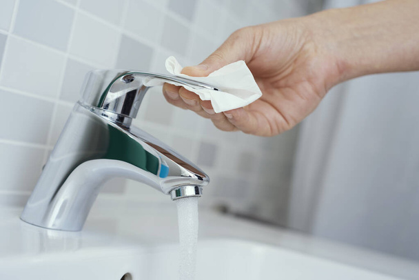 Enfeksiyonların bulaşmasını önlemek için parmaklarını bir parça kağıtla kaplayan musluğa dokunan beyaz bir adamın yakın çekimi. - Fotoğraf, Görsel