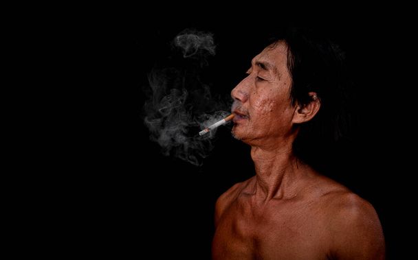 Het portret slanke oude man was roken op de zwarte achtergrond, Afbeelding van sigarettenrook verspreid in de mond concept - Foto, afbeelding