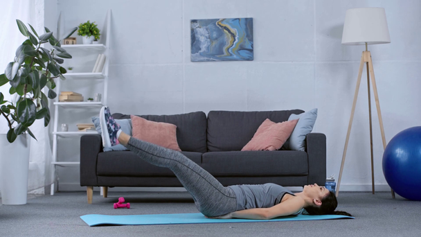 Side view of sportswoman working out on fitness mat in living room - Materiaali, video