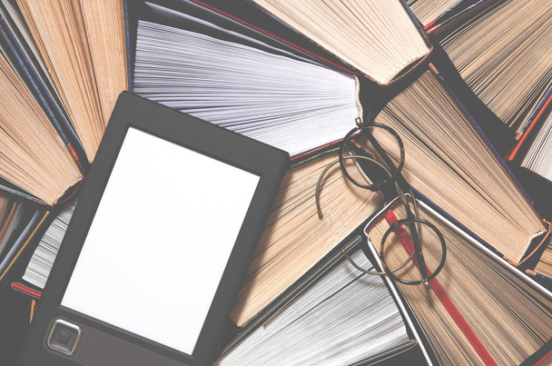 Das E-Book mit weißem Bildschirm liegt auf den offenen mehrfarbigen Büchern, die auf einem dunklen Hintergrund liegen, bereit zum Lesen. Nahaufnahme - Foto, Bild