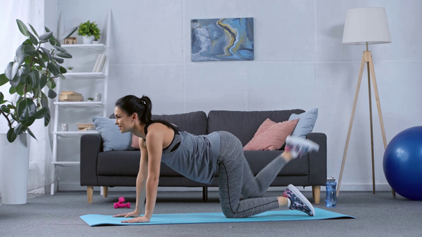 Vista lateral de la deportista sonriente haciendo ejercicio en la alfombra de fitness en casa
 - Imágenes, Vídeo