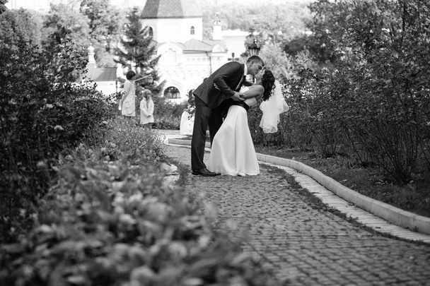 Красивий наречений нахиляється і обіймає наречену в парку
 - Фото, зображення