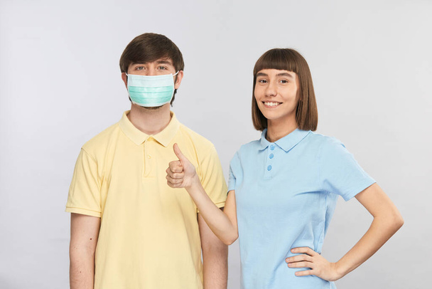 保護マスクをした可愛い若い男と笑顔で親指を立てる可愛い女の子伝染病や大気汚染中に滅菌マスクを着用 - 写真・画像