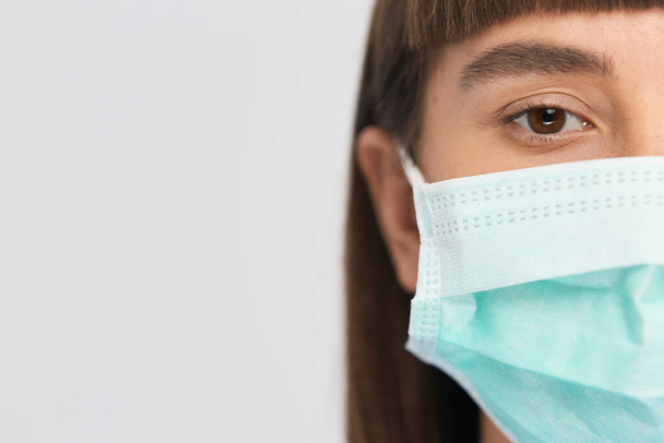 наполовину женщина лицо в защитной стерильной маске с глазом, глядя в камеру, скопировать пространство, коронавируса пандемии защитное лицо
 - Фото, изображение