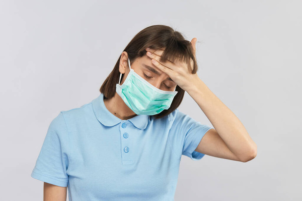 exhausted sick young woman touching with arm her forehead wearing sterile disposable mask - Photo, Image