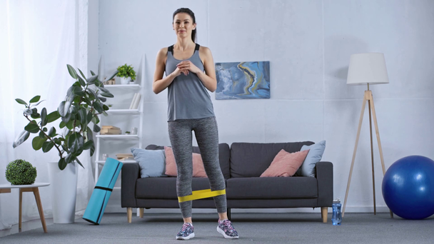 Спортивна жінка тренує ноги з опором у вітальні
 - Кадри, відео