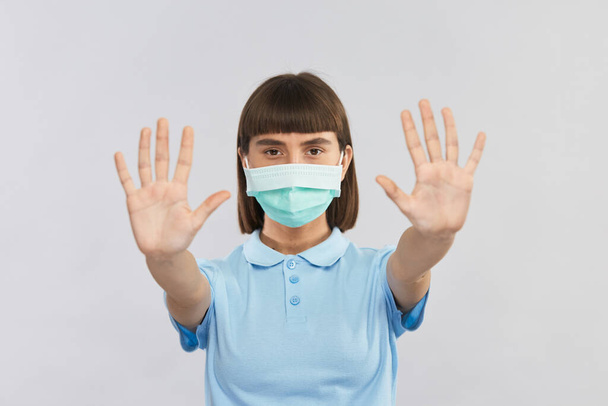 young strong woman in sterile mask showing social distancing with stop gesture of her arms - Photo, Image