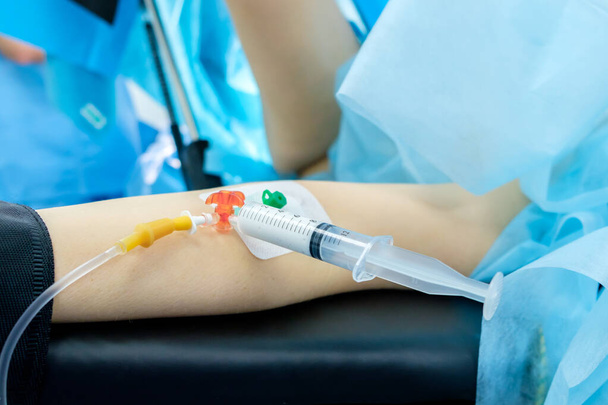 A catheter with a syringe in the hand of a patient lying on an operating table. The process of surgery under general anesthesia. Anesthesia is administered through a syringe. The patient is sleeping. - 写真・画像