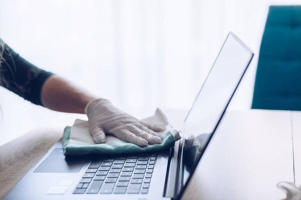 Mujer desinfecta el teclado portátil con líquido desinfectante en aerosol
 - Foto, imagen