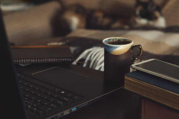 Otthoni iroda koncepció. Laptop, egy csésze kávé az asztalon és egy macska a háttérben - Fotó, kép