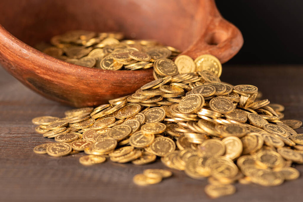 Cascata de pequenas moedas de ouro de um pote de barro
 - Foto, Imagem