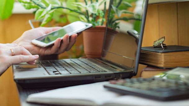 Otthoni iroda koncepció. Egy nő dolgozik egy laptopon, okostelefont tart a kezében. - Fotó, kép