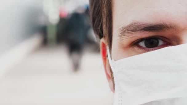 Μάτι που αναβοσβήνει με ένα δάκρυ ενός άνδρα σε μια ιατρική μάσκα για την προστασία από τον ιό COVID-19 coronavirus - Πλάνα, βίντεο