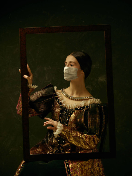 Medieval young woman as a duchess wearing protective mask against coronavirus spread - Photo, Image