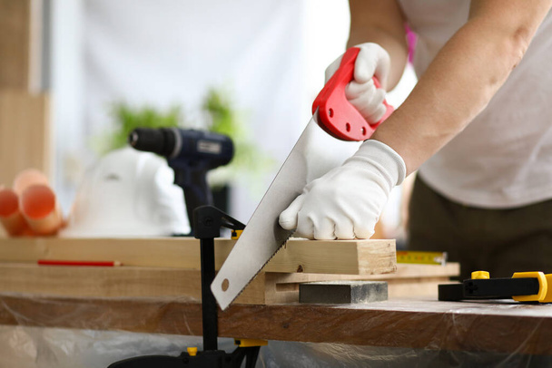 Gloved carpenter uses transverse sawing fixed part - Foto, imagen