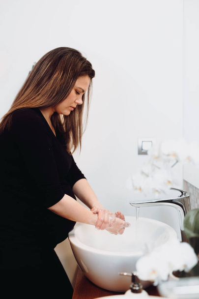 Bella donna incinta che si lava le mani a casa con disinfettante e sapone, acqua di rubinetto e cosmetici per la pulizia
 - Foto, immagini
