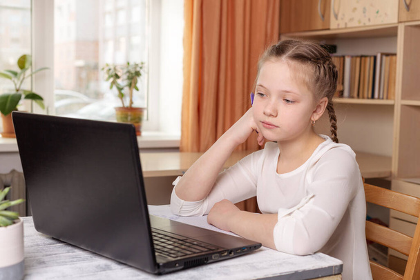 Serious schoolgirl looks at a laptop screen. Distance learning online education, home school, home education, quarantine concept - Image - Zdjęcie, obraz