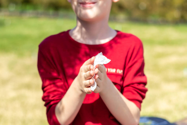 das Kind im roten T-Shirt, das seine Hände mit einem antibakteriellen Wischtuch reinigt. Außenschutzkonzept - Foto, Bild