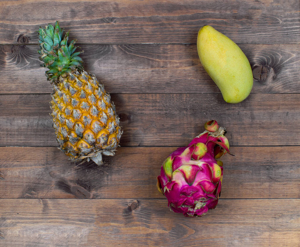 Exotic asia fruits on brown wood background. Assorted tropical summer fruits. Mango, dragon fruit, pitahaya and pineapple. The fresh fruits flat lay. - Fotó, kép