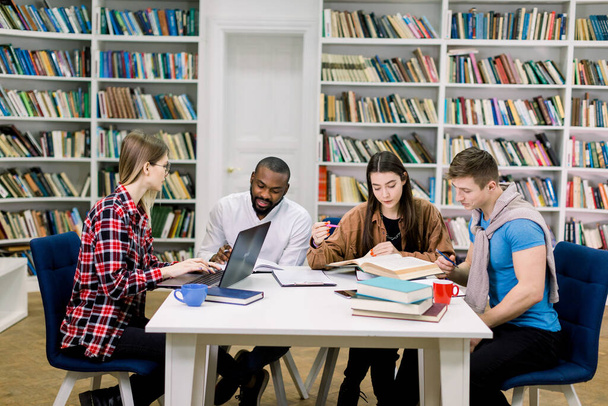 Education and learning concept. Multiethnic group of concentrated attractive diverse university students sitting at the table and preparing together for the exams in modern library - Foto, Imagem