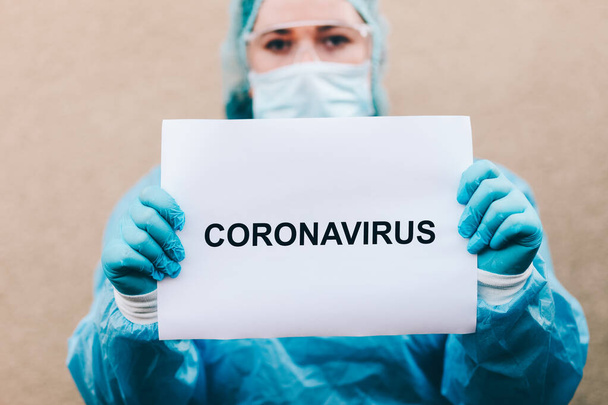 Frau im Schutzanzug hält Schild mit Coronavirus in der Hand - Foto, Bild
