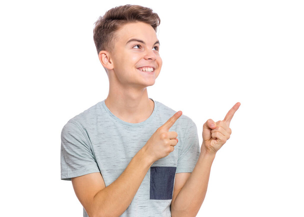 Portrait of teen boy pointing fingers away at copyspace, isolated on white background. Cute caucasian young teenager smiling and attracted by attention pointing fingers at something. Happy child. - Foto, Imagen