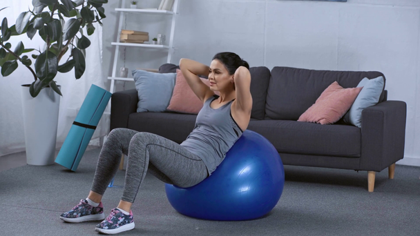 Bonita esportista fazendo abdominais na bola de fitness em casa
 - Filmagem, Vídeo