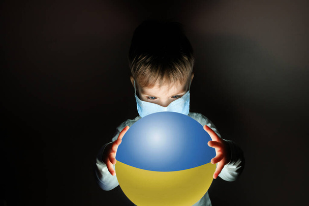Dünya gezegenini elinde tutan tıbbi maskeli şirin bir çocuk. Ukrayna 'da Coronavirus. covid-19 kavramı. - Fotoğraf, Görsel