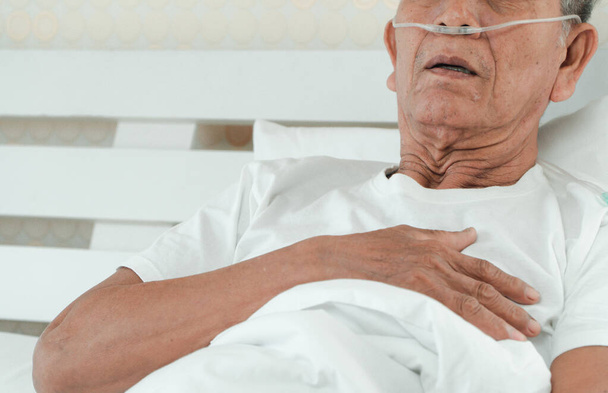 Sad senior man lying on the hospital bed and with a nasal breathing tube for treatment respiratory. Concept of Health care for the elderly, quarantine coronavirus (COVID-19) - Foto, Imagen