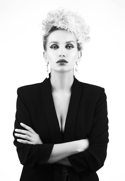 A beautiful blonde girl with an elegant hairstyle and large breasts, wearing a bra, trousers and a blazer, poses isolated on white. Trendy, commercial, monochrome, black and white, noir design - Photo, Image