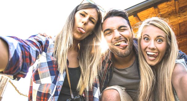 Friends trio taking selfie at trekking excursion - Happy friendship and freedom concept with young millenial people having fun together with funny faces on outdoors experience - Warm backlight filter - Foto, afbeelding