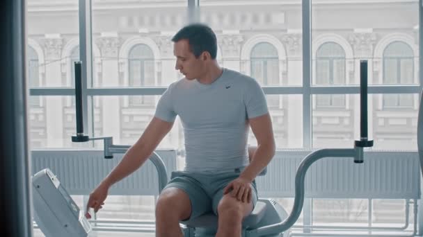 Σύγχρονο γυμναστήριο - ένας τύπος κάθεται στη συσκευή κατάρτισης και περιμένει πότε θα είναι δυνατόν να ξεκινήσει - Πλάνα, βίντεο