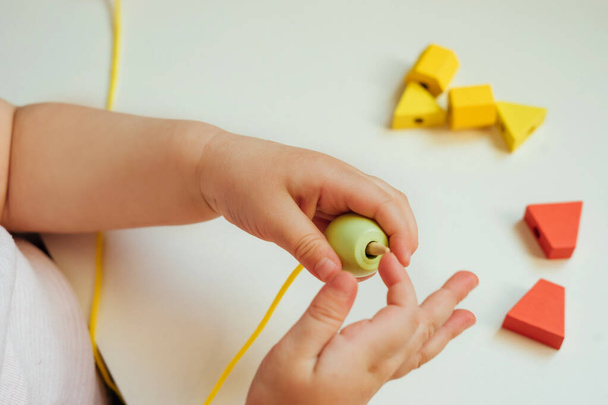 Child putting beads on a string. Bead stringing activity. Fine motor skills development. Early education, Montessori Method. Cognitive skills, children development. Close up of baby's hands. Lacing, threading activities.  - Photo, Image